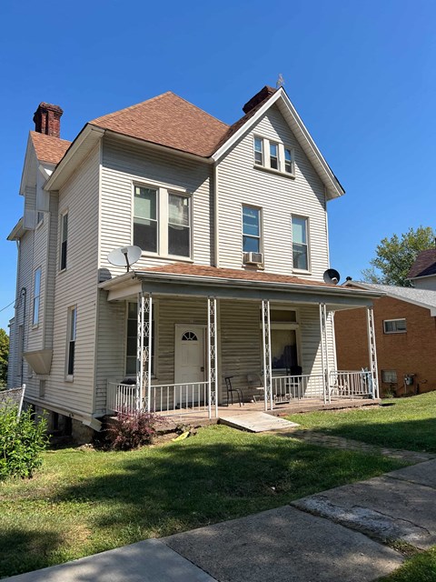 A two-story house with a porch and a satellite dish on the roof.