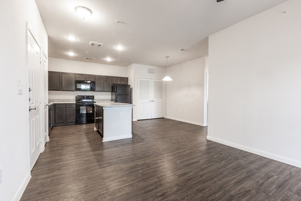 an empty living room and kitchen with wood flooring and white walls