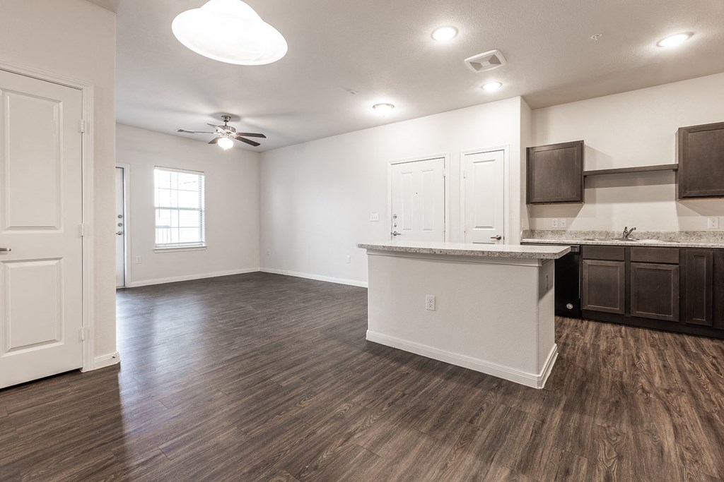 an empty living room with a kitchen and a ceiling fan