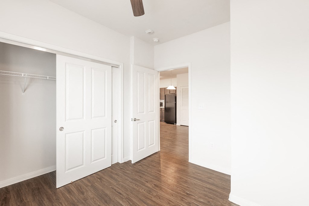 a bedroom with white walls and wood floors and a closet