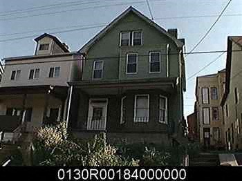 A green house with a white window is in front of a tan house.