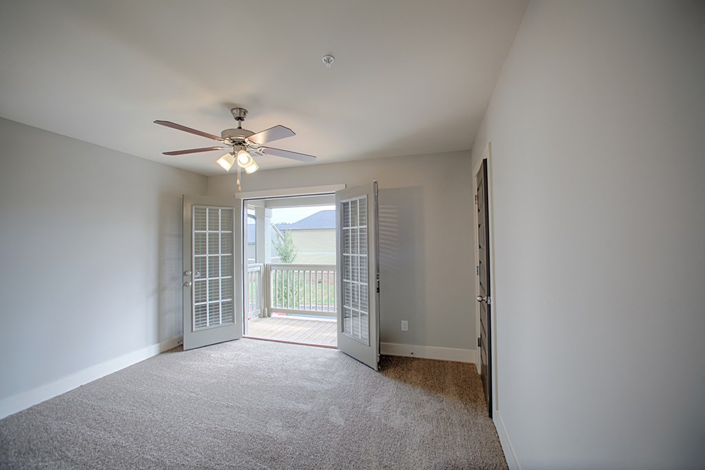 an empty living room with a ceiling fan and a balcony