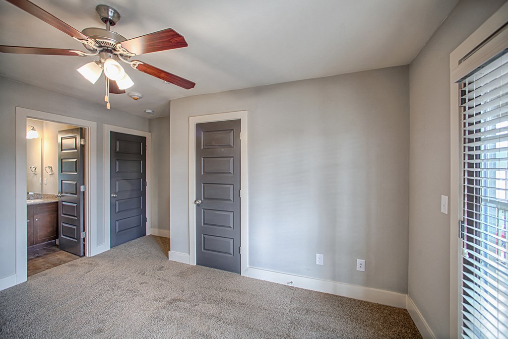 an empty living room with a ceiling fan and a door to a bathroom