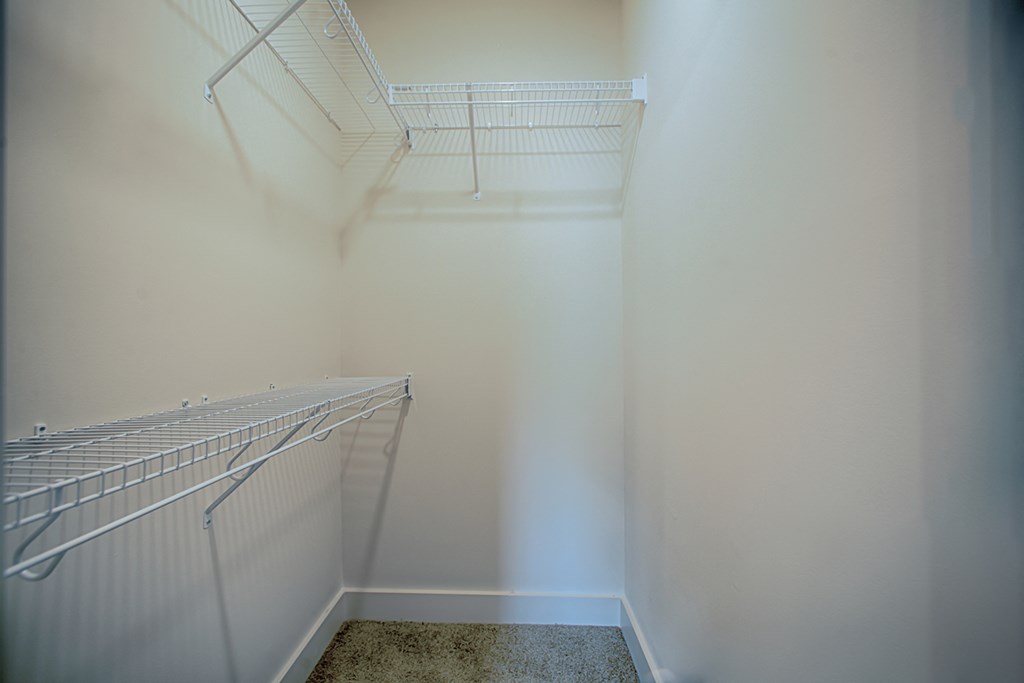 a walk in closet with two white shelves and a white wall and a carpet