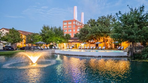A fountain in the middle of a pond in front of a building.