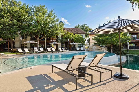 A poolside area with sun loungers and a striped umbrella.