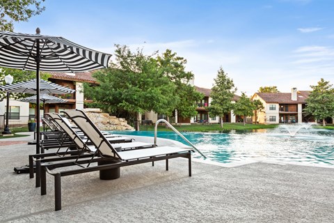 A pool with a waterfall and lounge chairs.