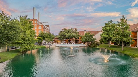 A serene lake with a fountain in the middle surrounded by buildings and trees.