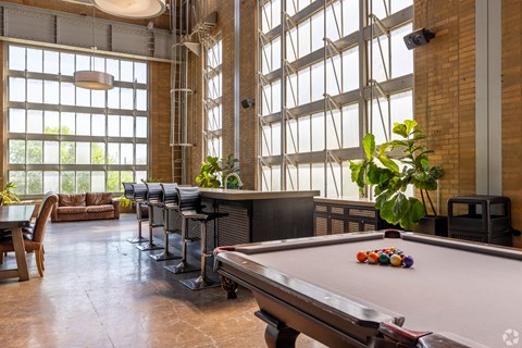 A pool table with balls in the corner of a room with a brick wall and large windows.