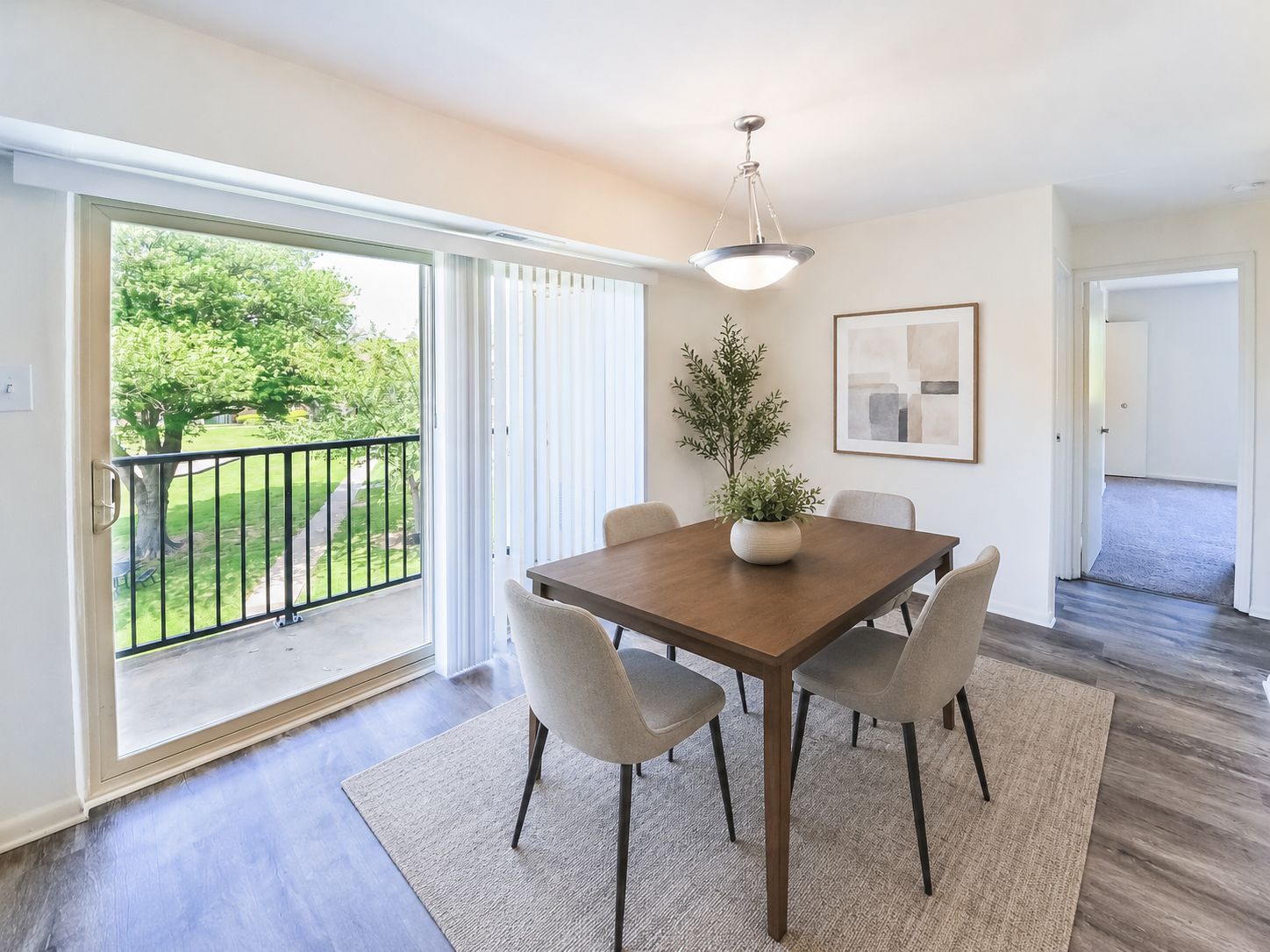 A dining room with a table and chairs and a view of a green lawn outside.