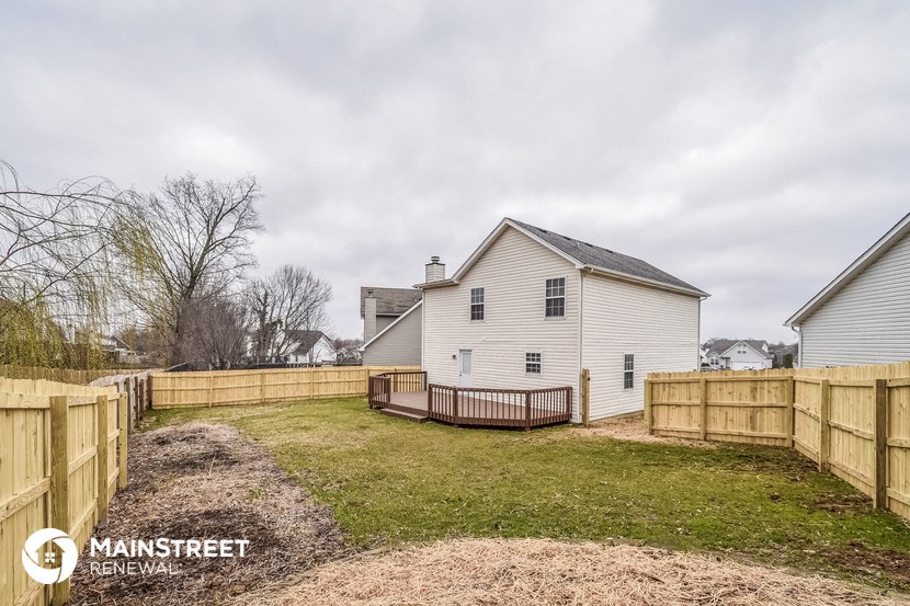 the back yard of a white house with a wooden fence