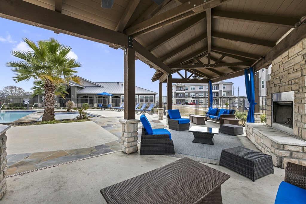 a covered patio with chairs and a fireplace next to a swimming pool