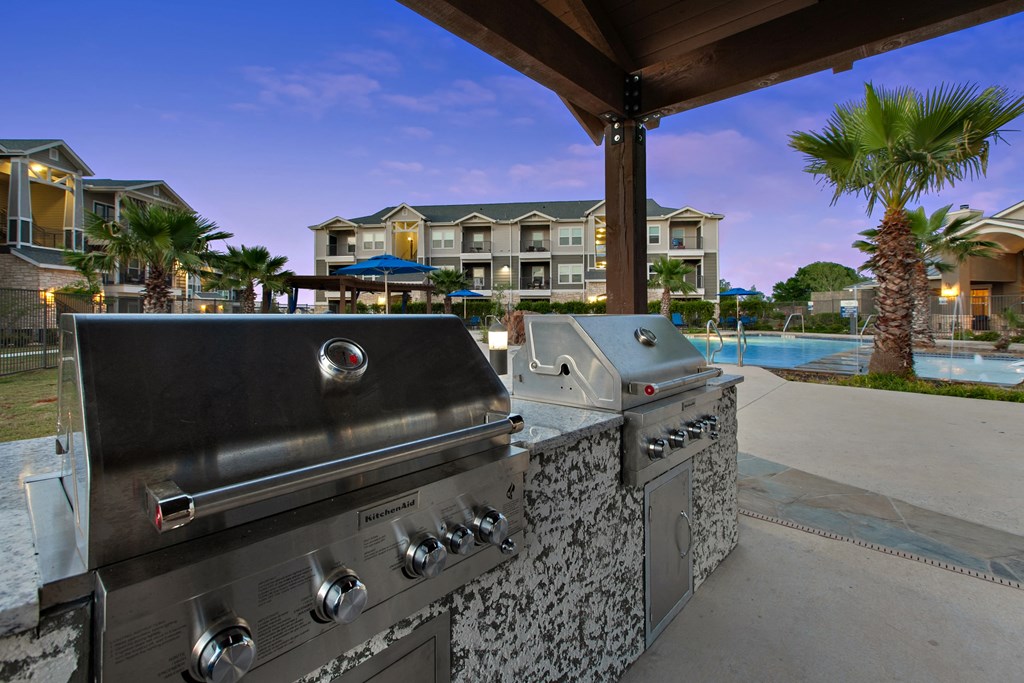two gas barbecue grills on a patio next to a swimming pool