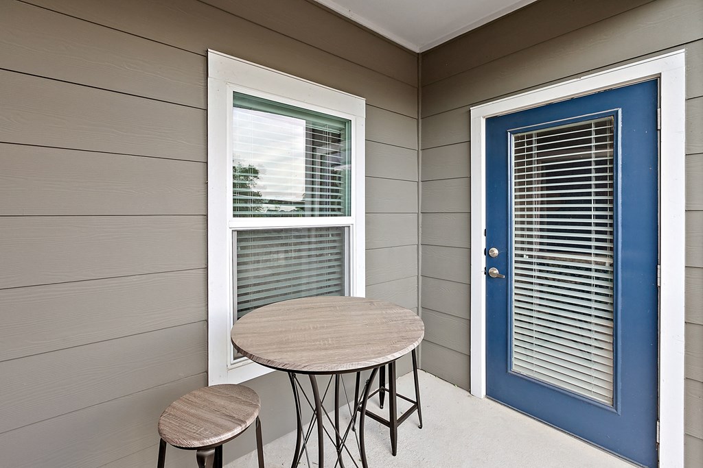 a patio with a table and two stools in front of a blue door