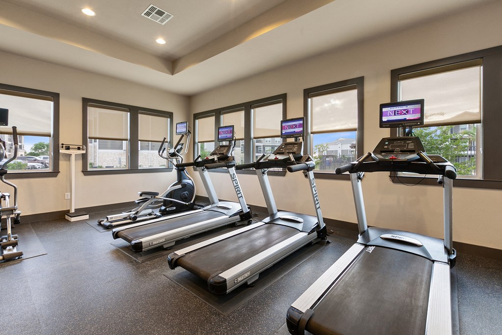 two treadmills and ellipticals in a gym with windows