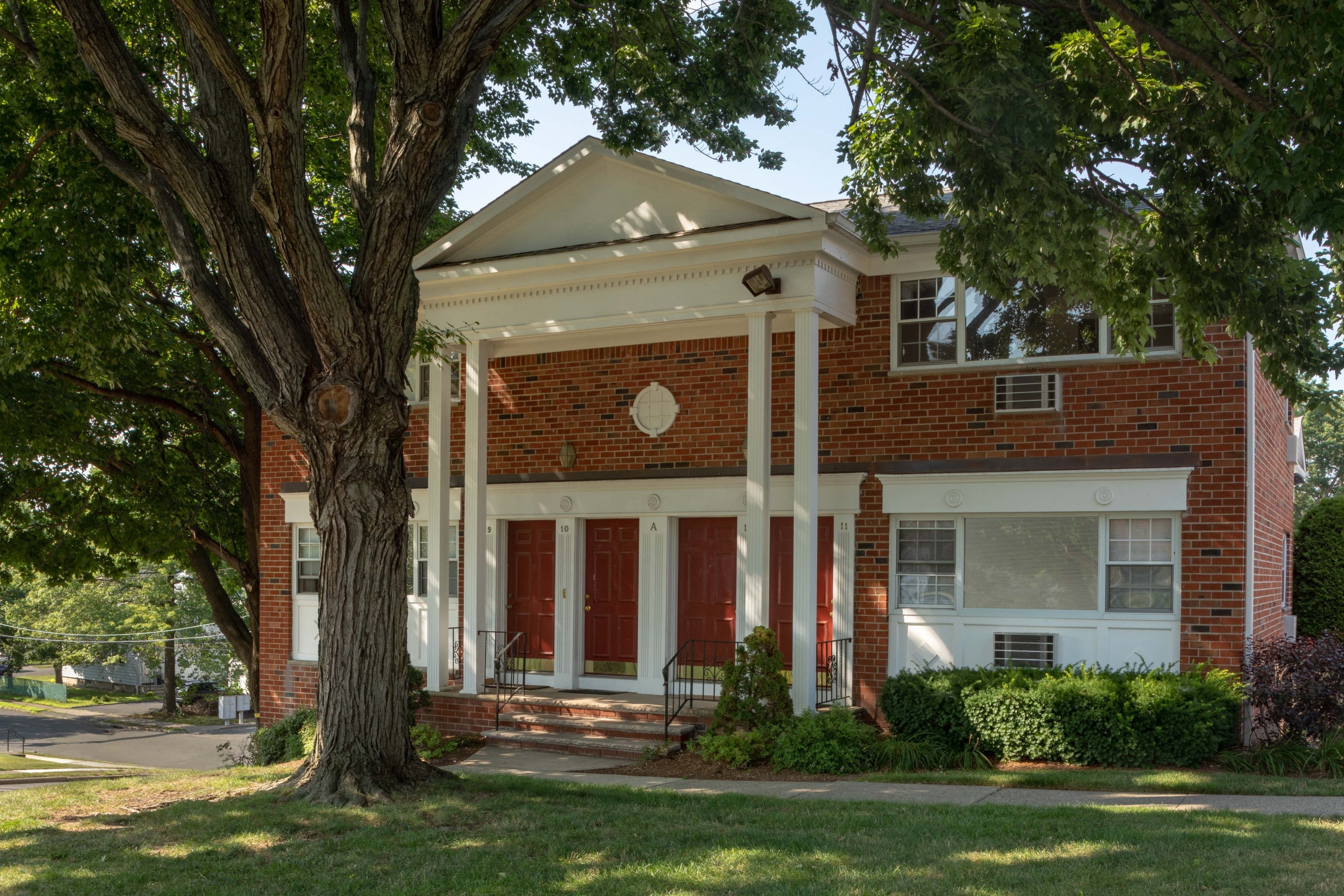 a red brick house with white columns and a large tree