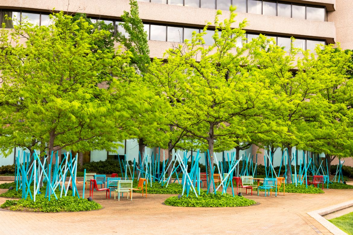 a seating area with trees and blue chairs in front of a building