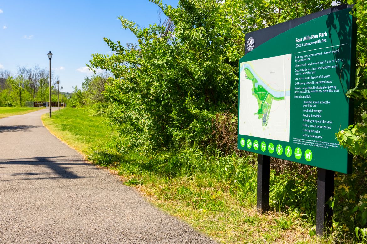 a sign for a park with green trees and a path