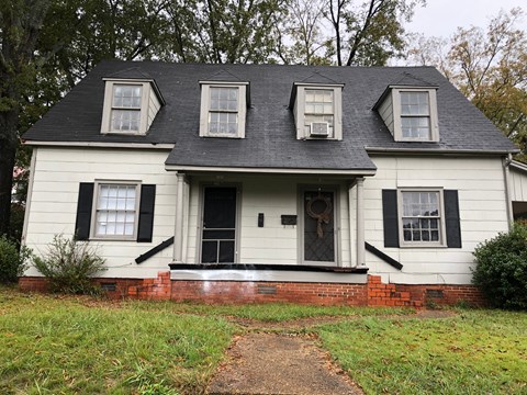 A white house with black shutters and a brick base.
