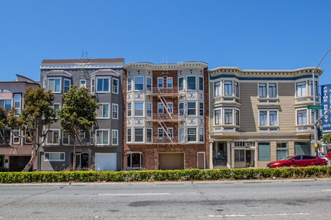 A row of three-story apartment buildings with balconies line a street.