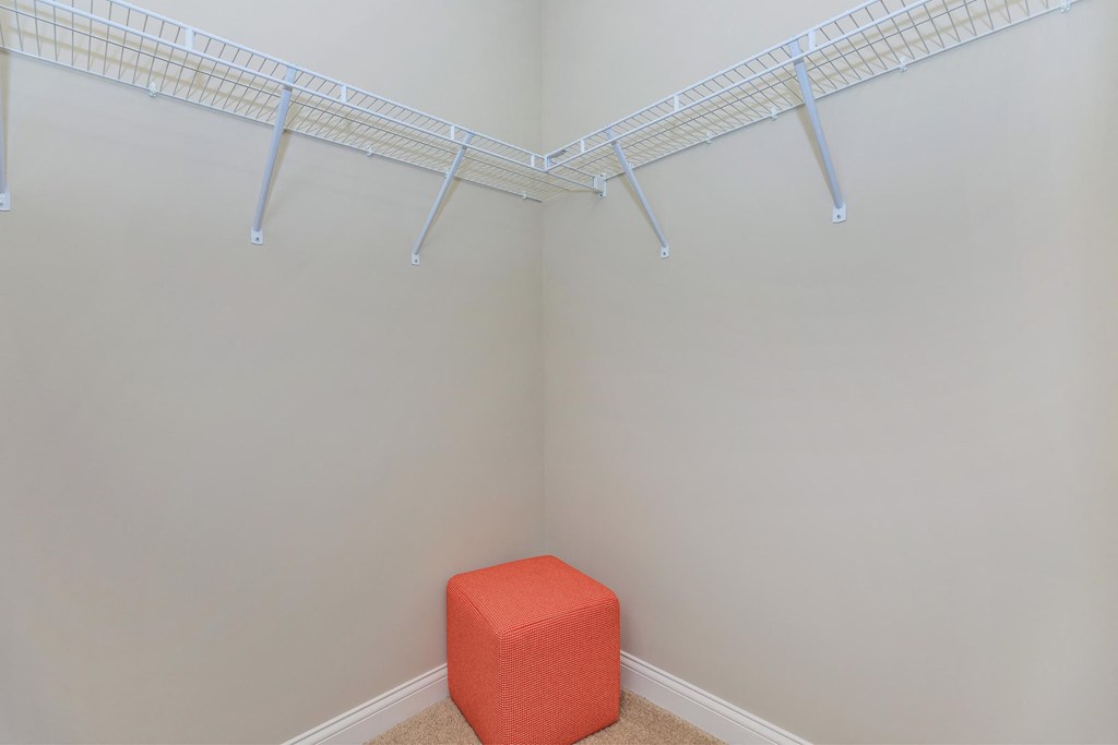 a walk in closet with an orange stool in the corner