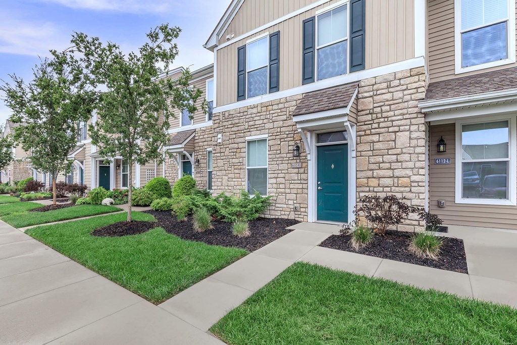 a sidewalk in front of a building with green grass and trees