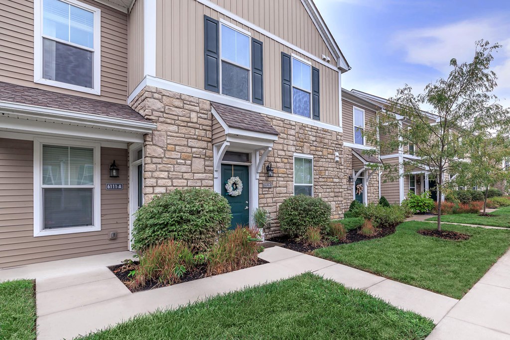 a sidewalk in front of a brick house with a green door