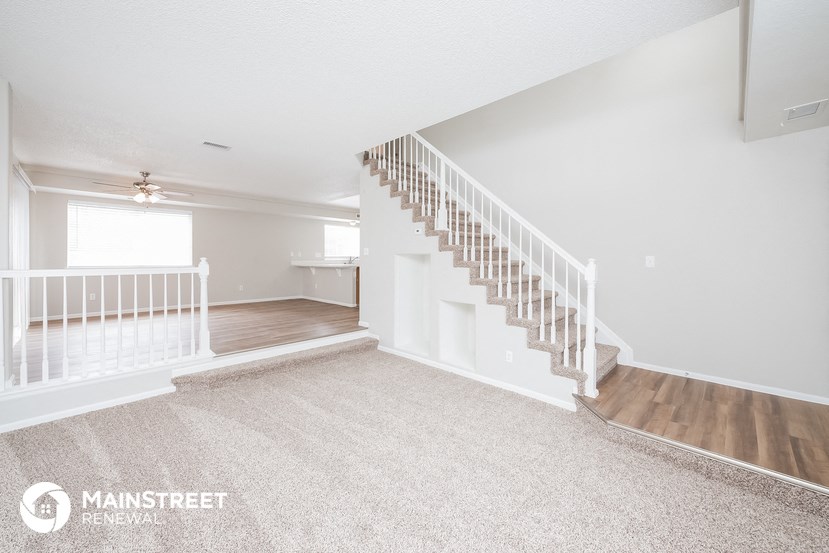 the upstairs of a white house with a staircase and a carpeted floor