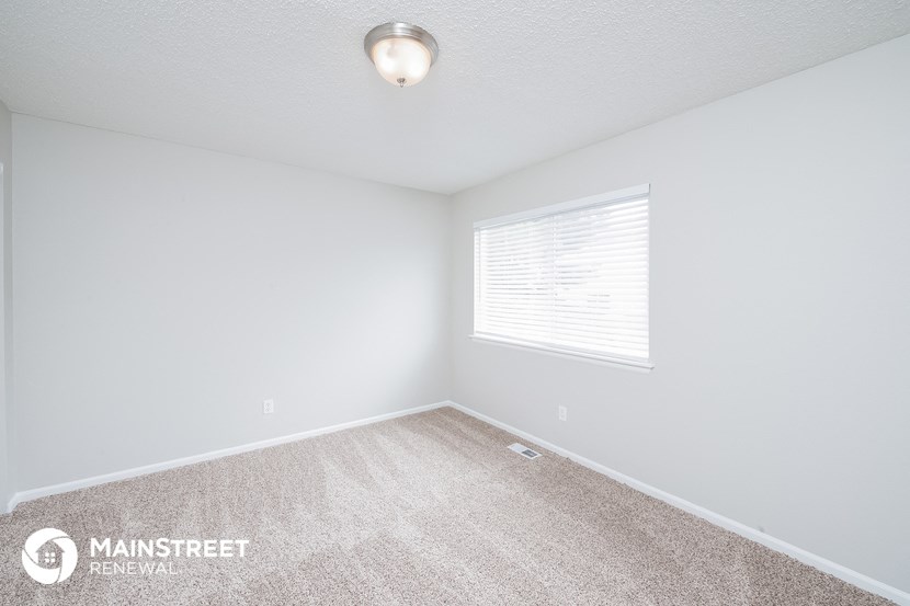 the spacious bedroom with carpeted flooring and a large window