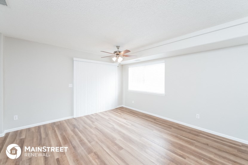 the spacious living room with wood flooring and a ceiling fan