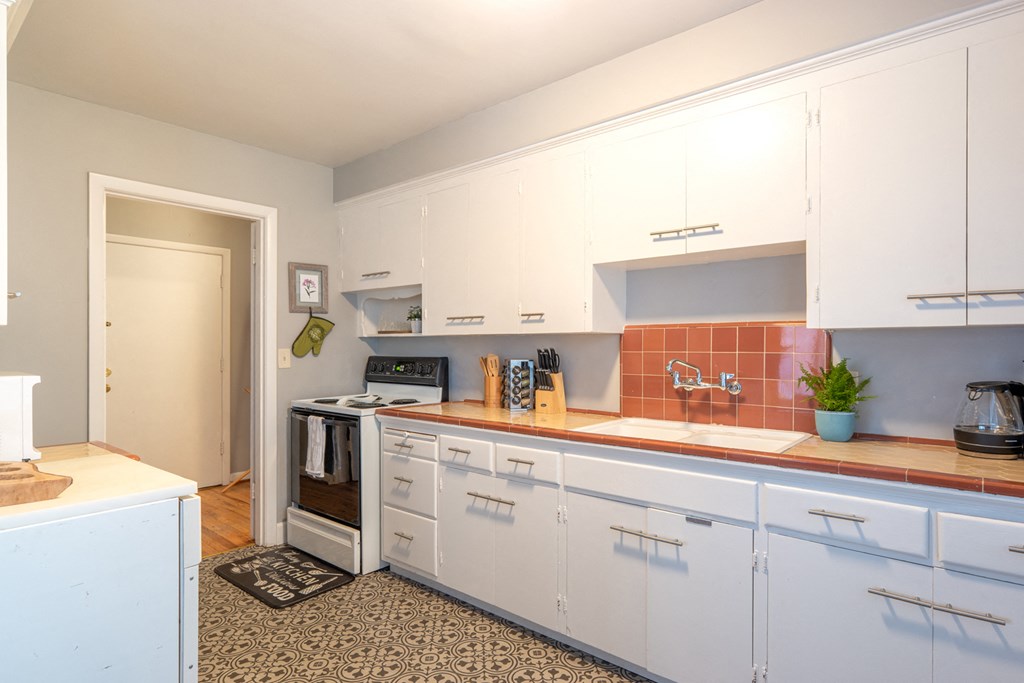 a kitchen with white cabinets and red countertops and a door to a living room