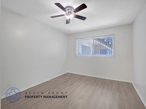 A room with a ceiling fan and a window with a view of a building outside.