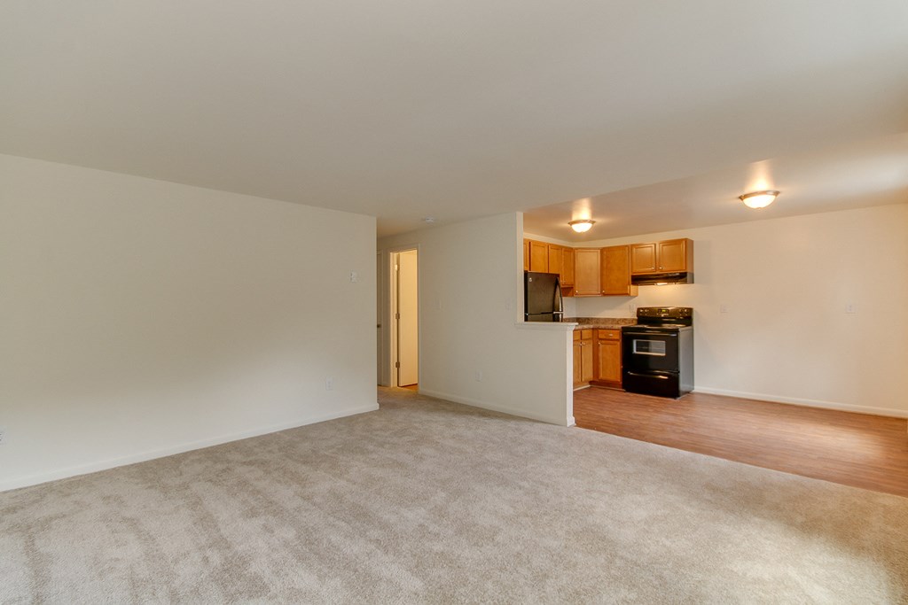 an empty living room with a kitchen in the background