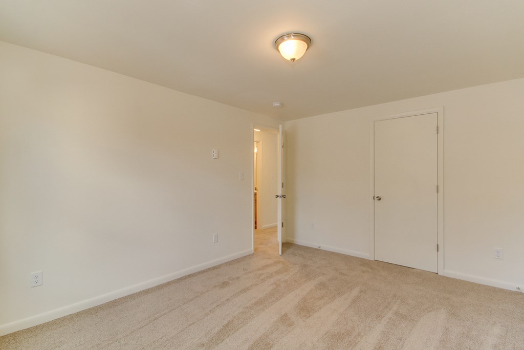 a bedroom with white walls and carpet and a door to a hallway