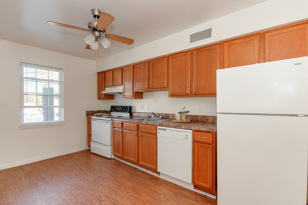 a kitchen with white appliances and wooden cabinets and a ceiling fan
