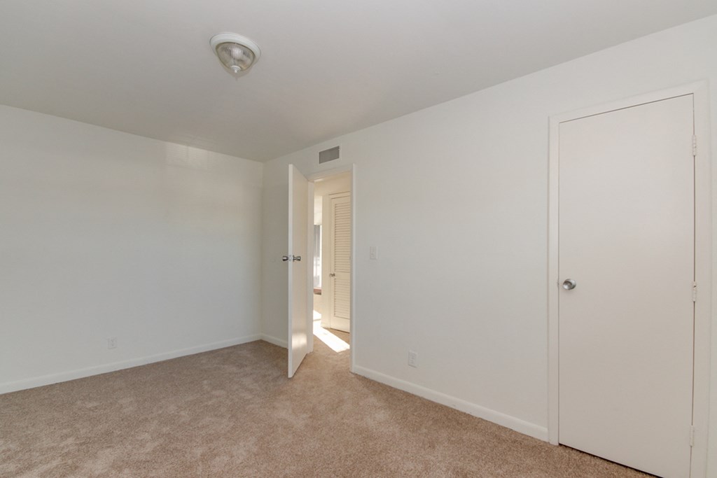 a bedroom with white walls and carpet and a door to a hallway
