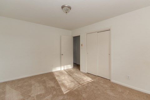 a bedroom with white walls and carpet and a door to a closet