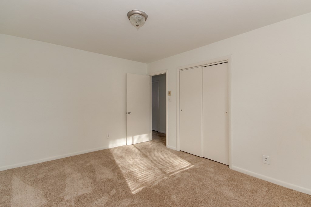 a bedroom with white walls and carpet and a door to a closet