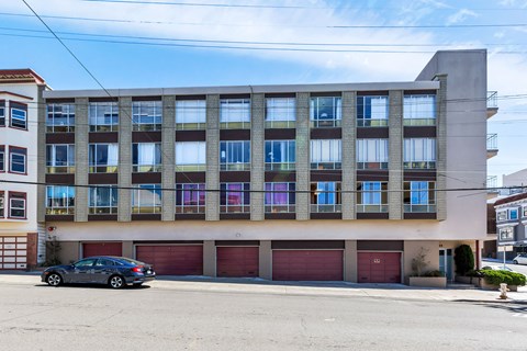 A car is parked in front of a building with red garage doors.