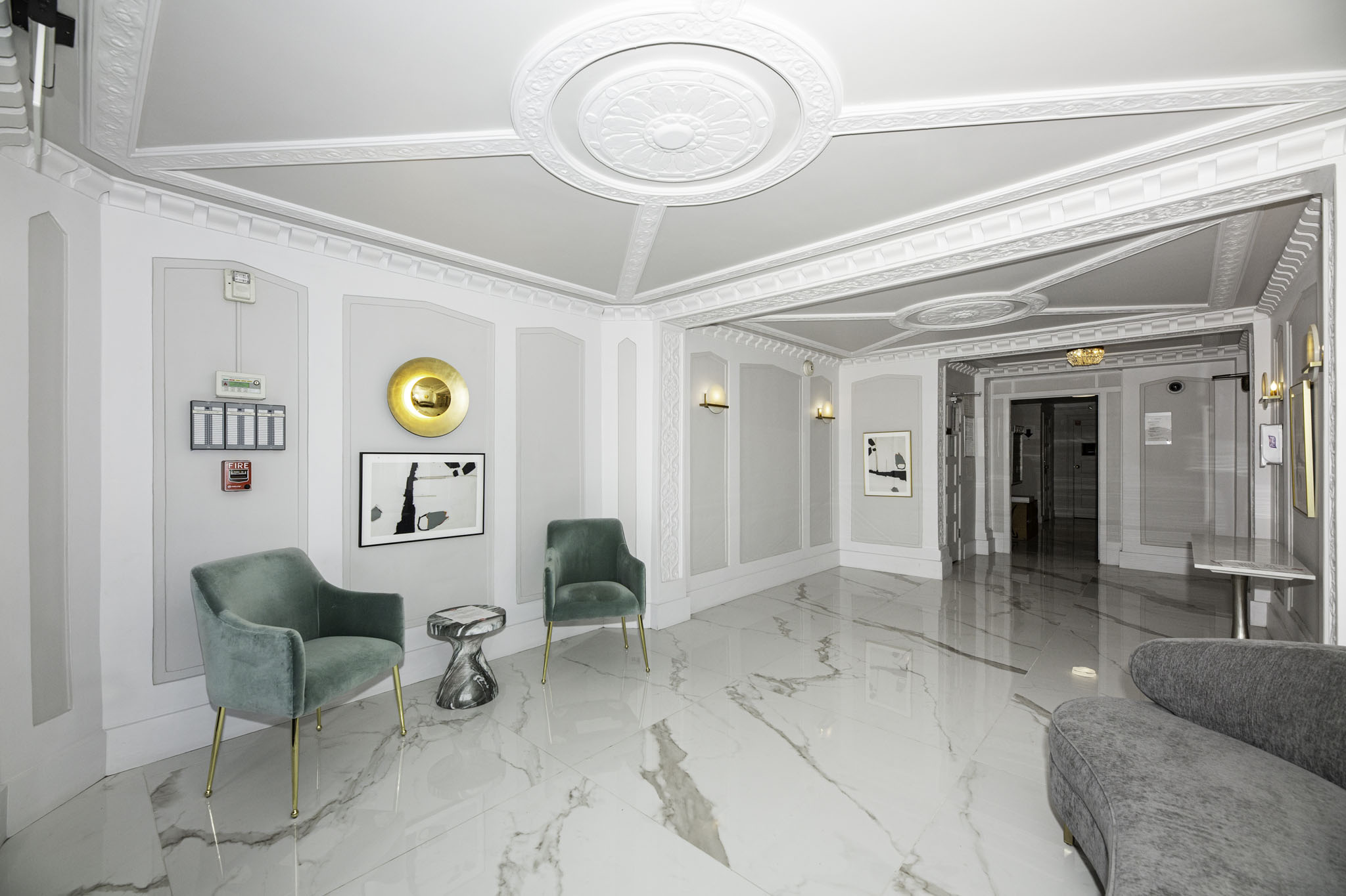 A white hallway with a green chair and a grey couch.