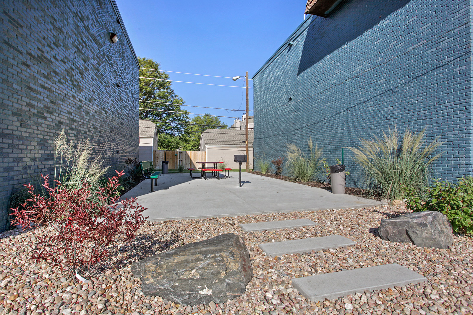a concrete walkway between two brick buildings with rocks and plants