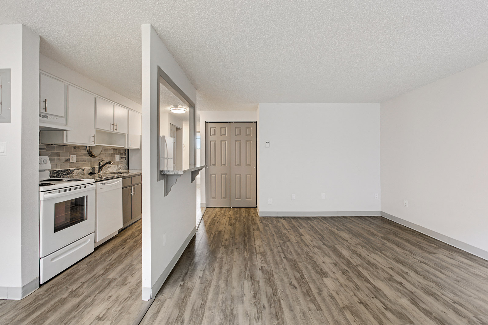an open kitchen and living room with white appliances and wood flooring