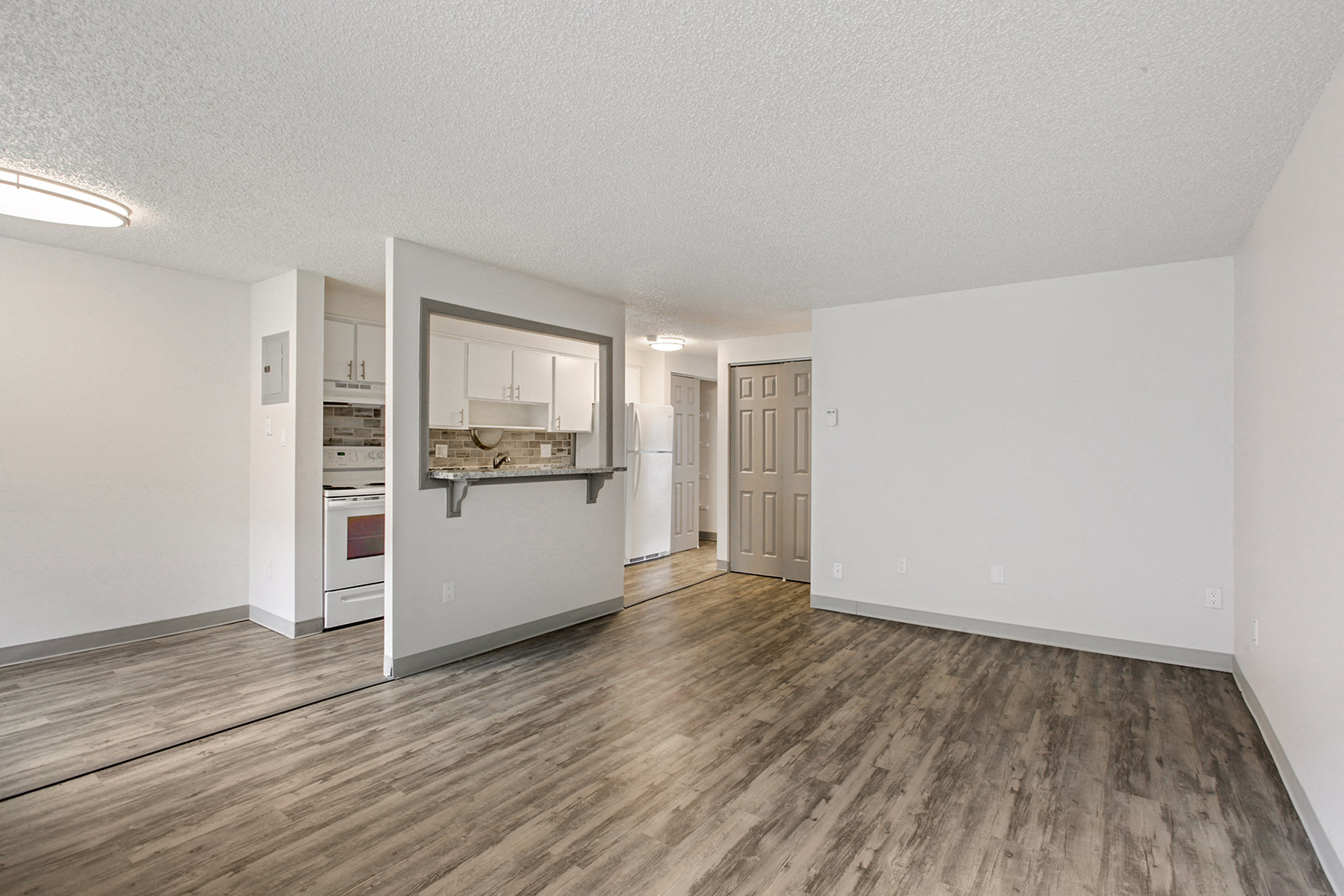an empty living room and kitchen with wood flooring and white walls