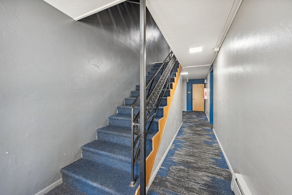 a long hallway with blue carpeted stairs and a blue door