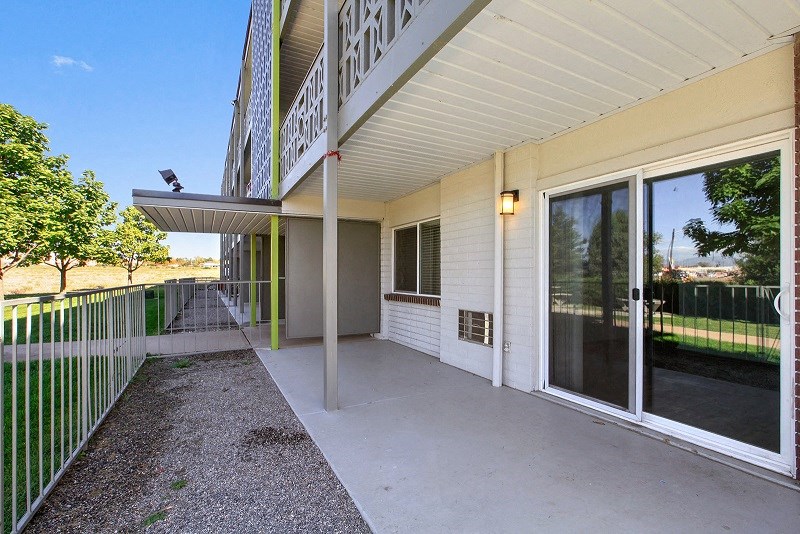 a long porch with a glass door and a green fence
