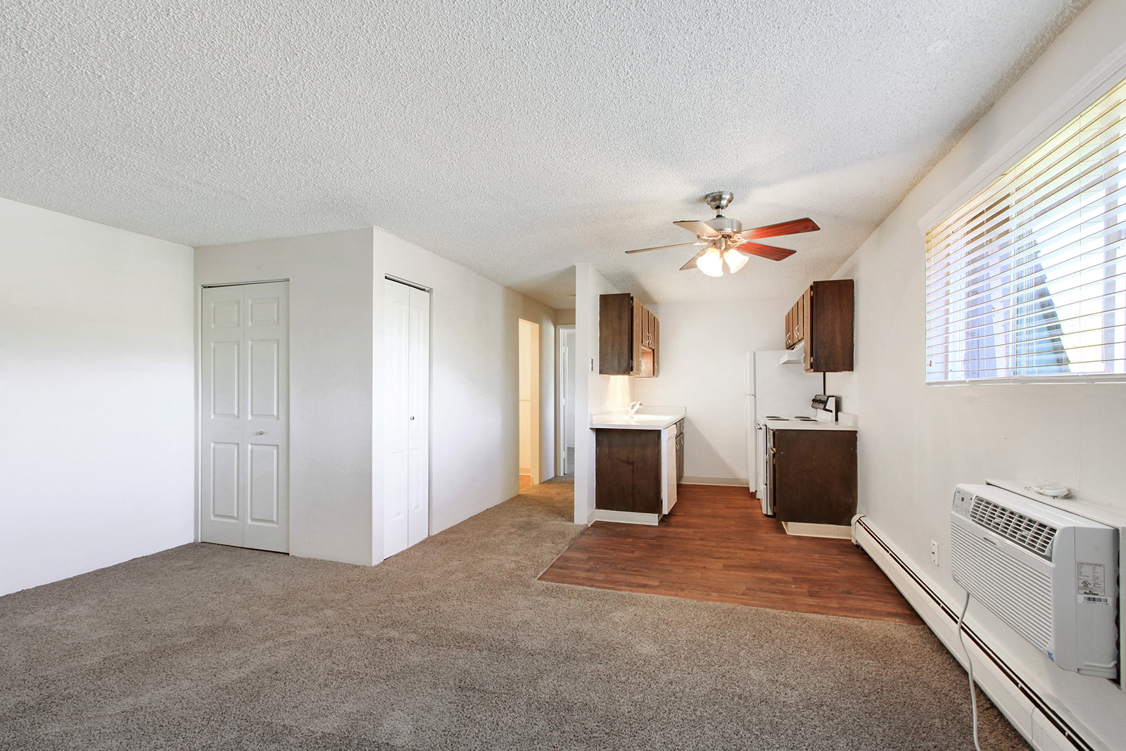 an empty living room with a ceiling fan and a kitchen