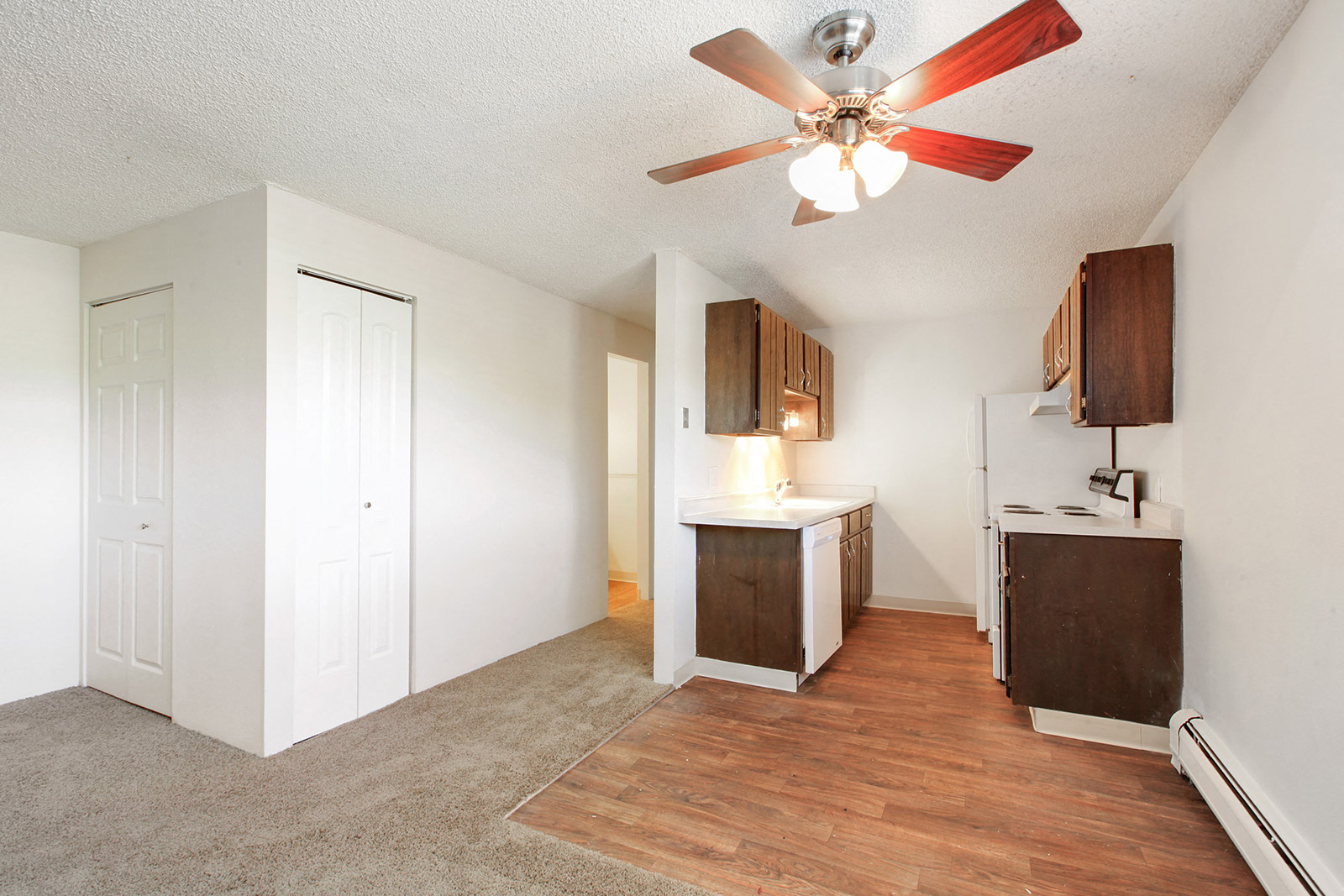 an empty living room with a ceiling fan and a kitchen
