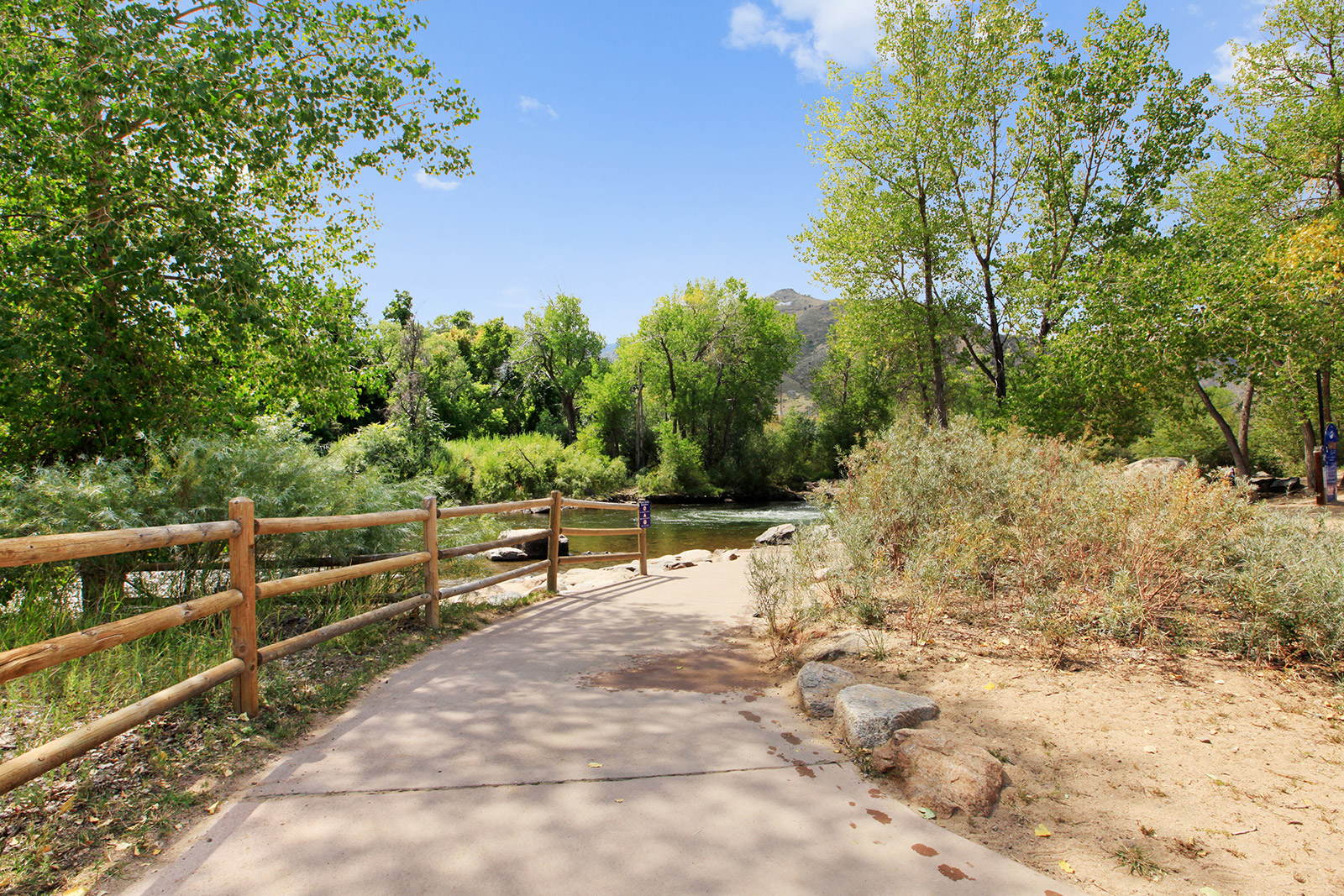 a path through a park with a river and a wooden fence