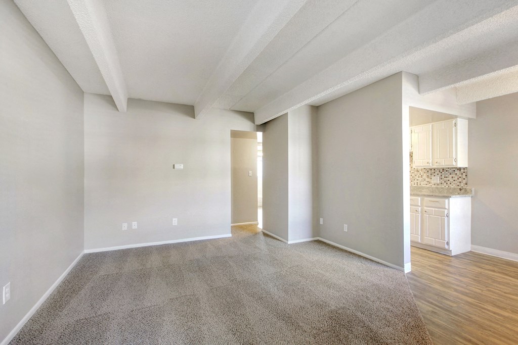 an empty living room with a kitchen in the background