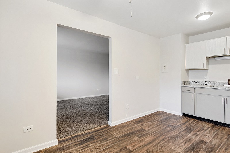 an empty kitchen and living room with white cabinets and wood flooring
